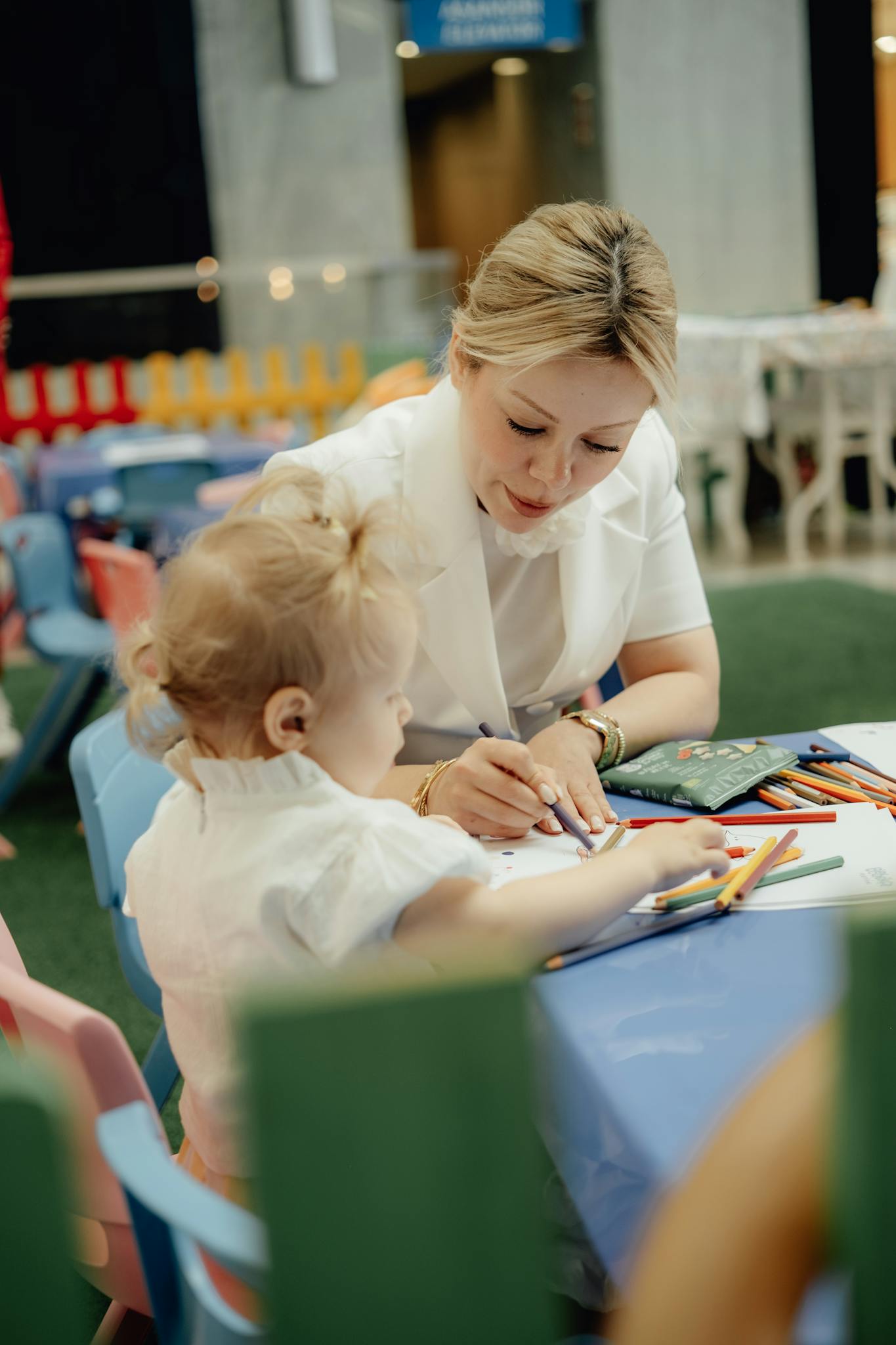 A loving mother helps her child draw at a colorful kindergarten setting.